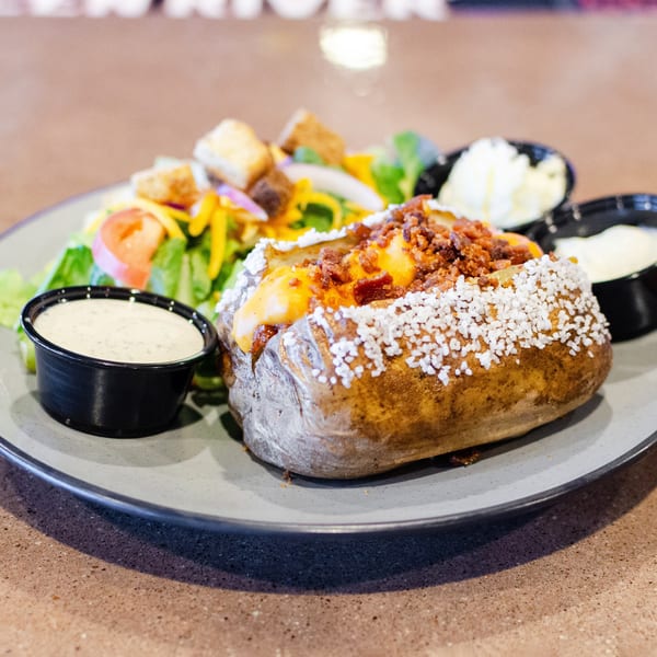 Loaded baked potato with cheese, bacon, and salt, served with a side salad and dressings.