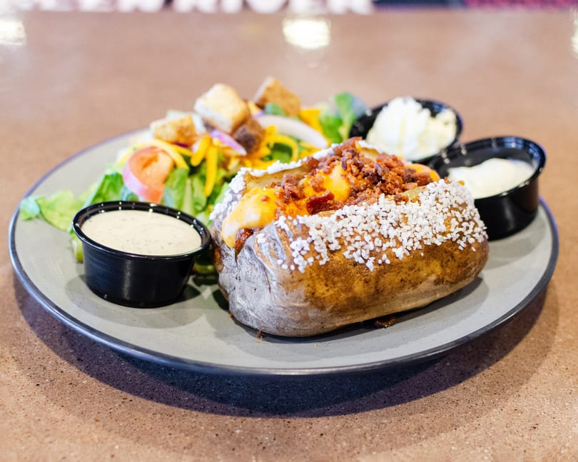 Loaded baked potato with cheese, bacon, and salt, served with a side salad and dressings.