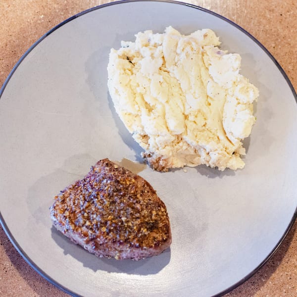 A seasoned steak and a scoop of mashed potatoes on a light gray plate.