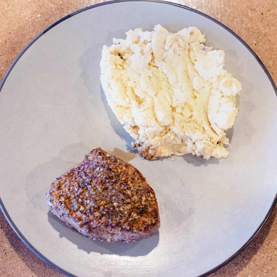 A seasoned steak and a scoop of mashed potatoes on a light gray plate.