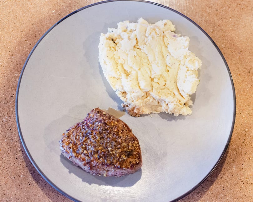 A seasoned steak and a scoop of mashed potatoes on a light gray plate.