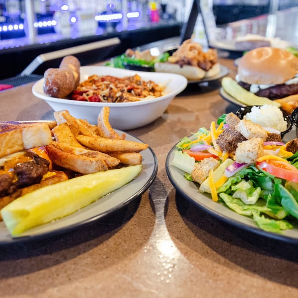 A table full of various dishes, including burgers, fries, salad, and pasta, at a restaurant.