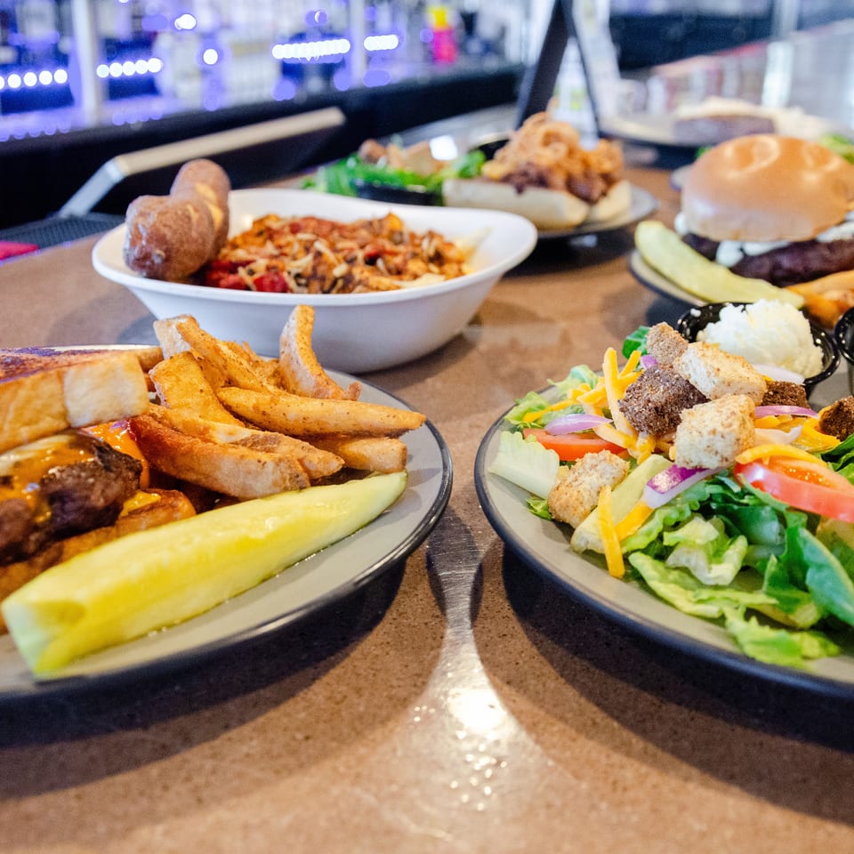A table full of various dishes, including burgers, fries, salad, and pasta, at a restaurant.