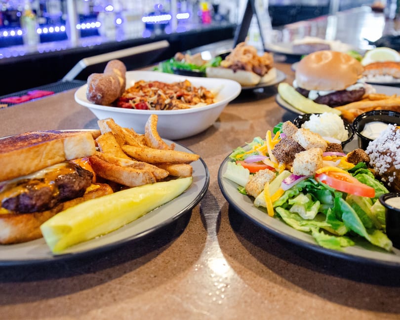 A table full of various dishes, including burgers, fries, salad, and pasta, at a restaurant.