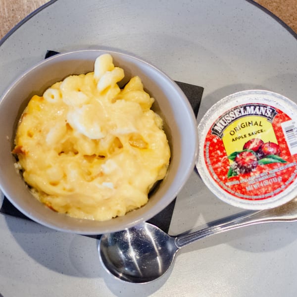 A bowl of macaroni and cheese with a side of Musselman's Original Apple Sauce and a spoon.