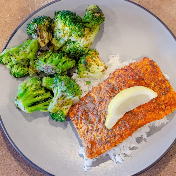 A plate of seasoned salmon with a lemon wedge, white rice, and roasted broccoli.