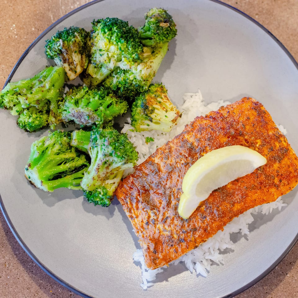 A plate of seasoned salmon with a lemon wedge, white rice, and roasted broccoli.