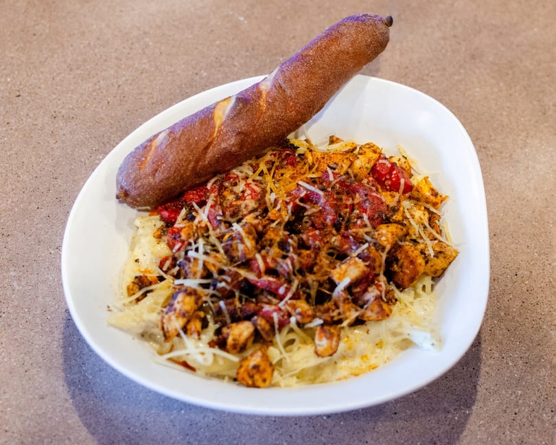 Creamy pasta topped with grilled chicken, red peppers, and shredded cheese, served with a breadstick.