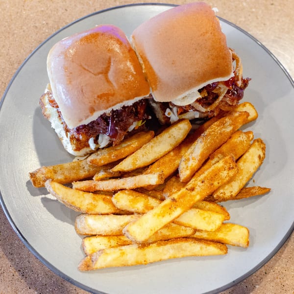 Two sliders with pulled pork and coleslaw, served with a side of seasoned french fries on a gray plate.