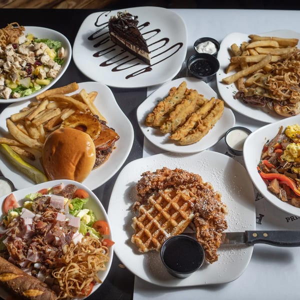 A table laden with various dishes including salads, burgers, fries, fried pickles, and dessert.