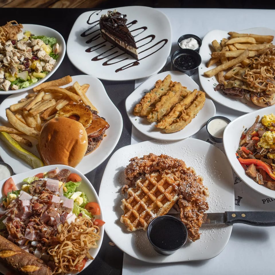 A table laden with various dishes including salads, burgers, fries, fried pickles, and dessert.