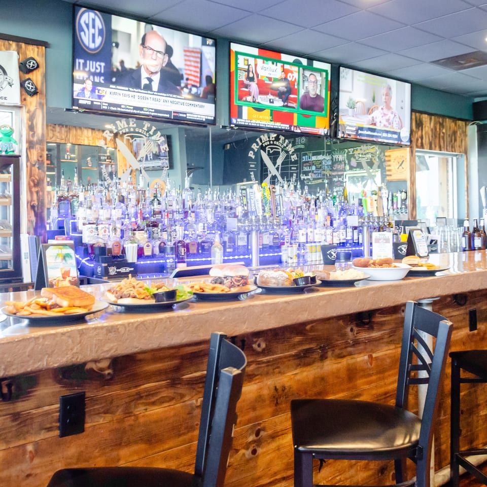A well-stocked bar with various food plates and three TVs showing different programs.