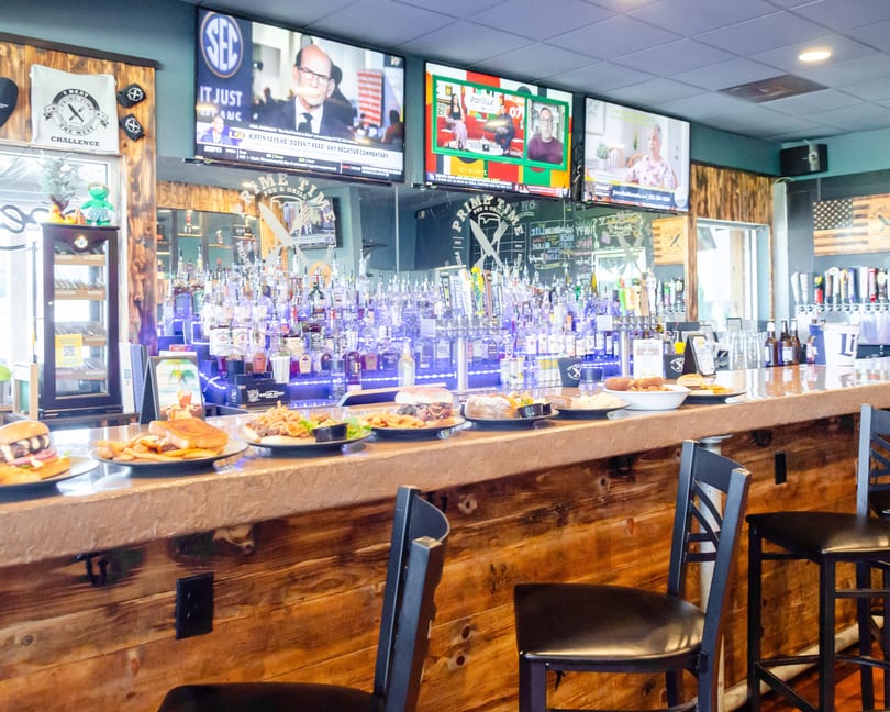 A well-stocked bar with various food plates and three TVs showing different programs.