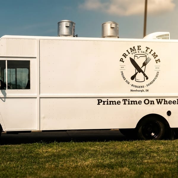 White Prime Time On Wheels food truck with a logo of a beer mug, knife, and fork.