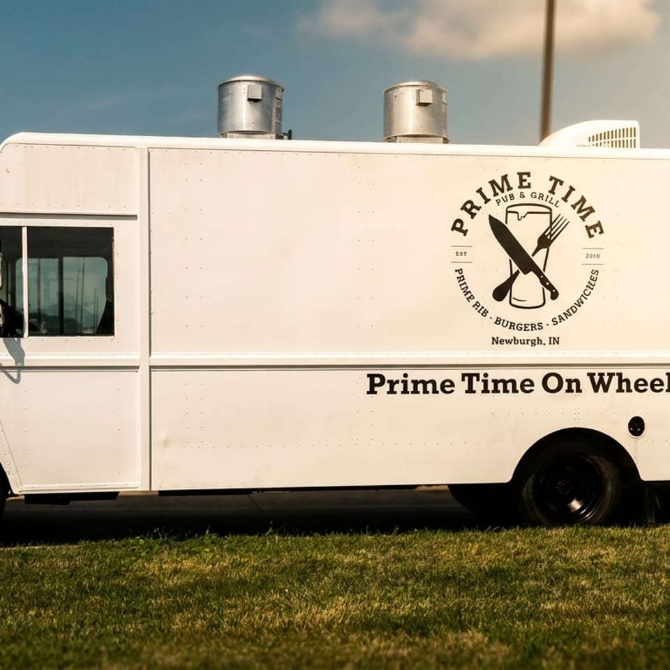 White Prime Time On Wheels food truck with a logo of a beer mug, knife, and fork.