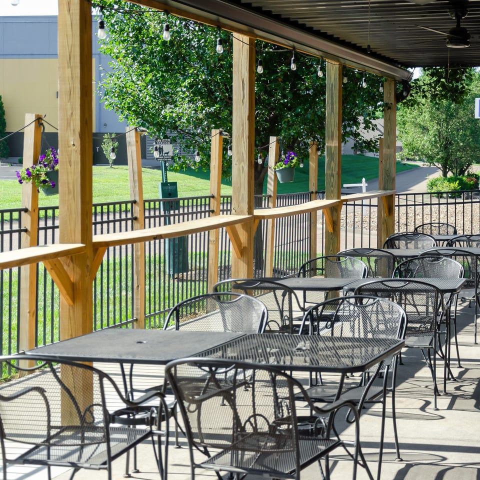 Outdoor patio with black metal tables and chairs under a covered pergola with string lights.