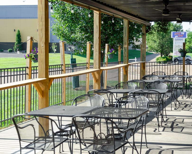 Outdoor patio with black metal tables and chairs under a covered pergola with string lights.