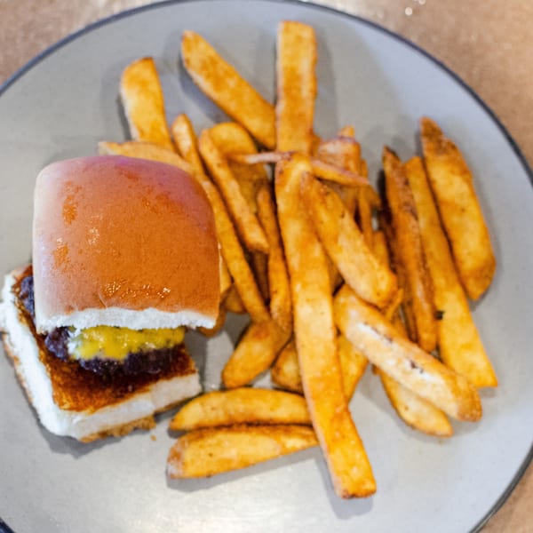 A slider with cheese and relish, served with a side of golden french fries on a gray plate.