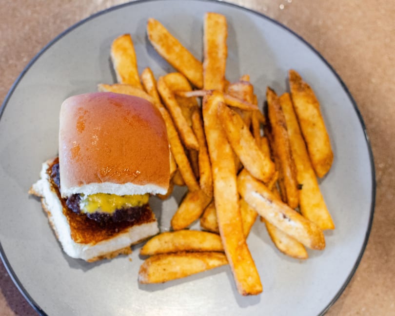 A slider with cheese and relish, served with a side of golden french fries on a gray plate.