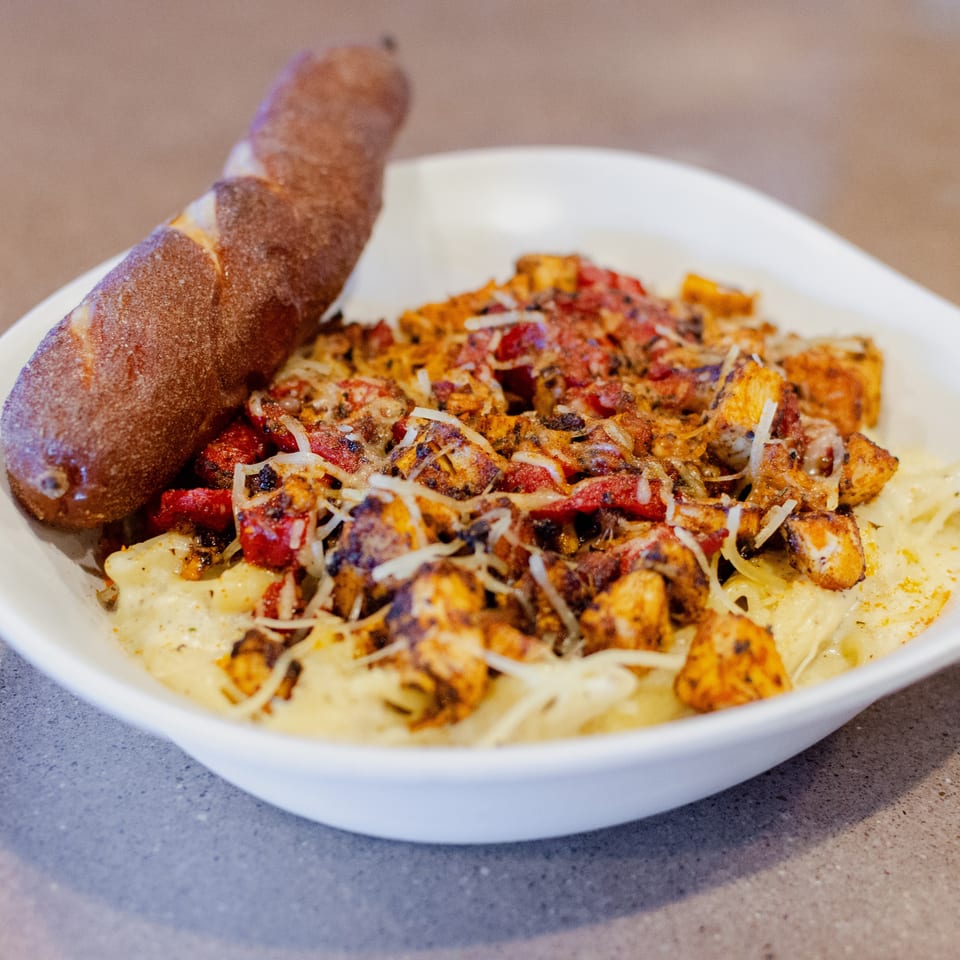Creamy pasta topped with grilled chicken, red peppers, and shredded cheese, served with a breadstick.