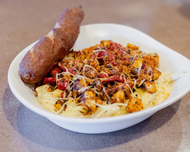 Creamy pasta topped with grilled chicken, red peppers, and shredded cheese, served with a breadstick.