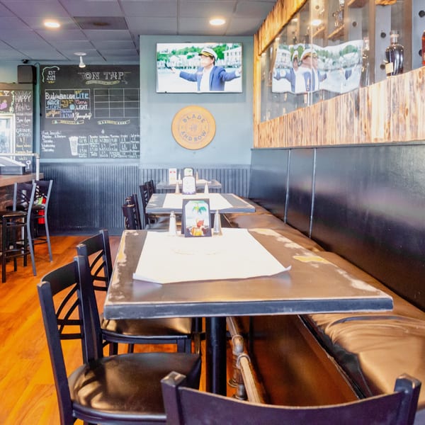 Interior of a restaurant with tables, chairs, a bar, and a TV playing a video.
