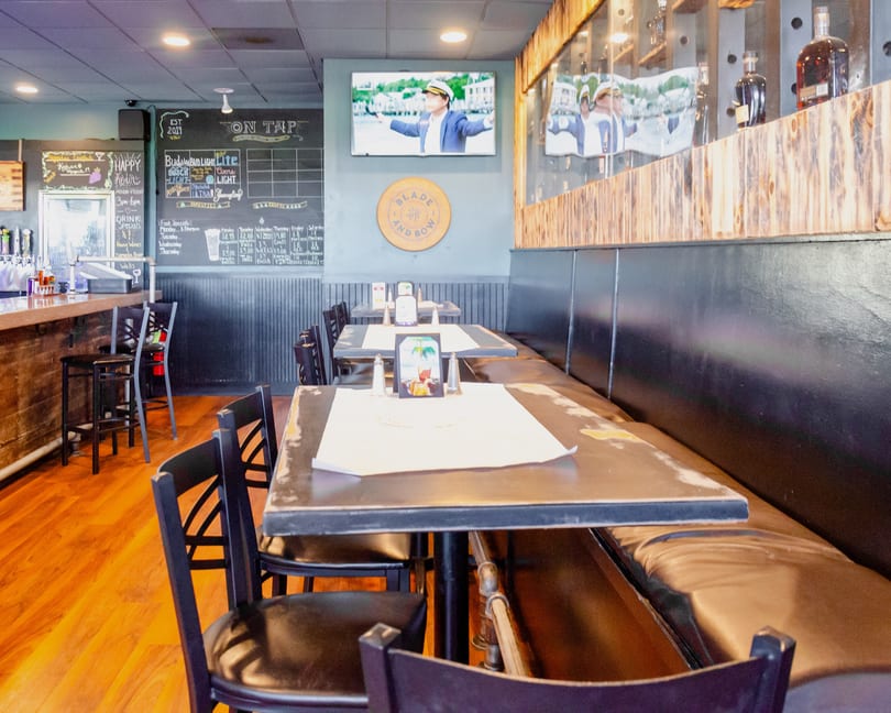 Interior of a restaurant with tables, chairs, a bar, and a TV playing a video.