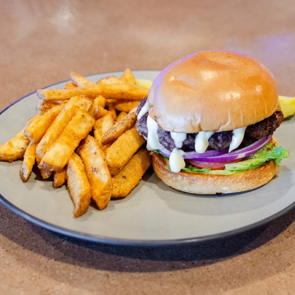 A juicy burger with lettuce, tomato, red onion, and white sauce, served with golden fries.