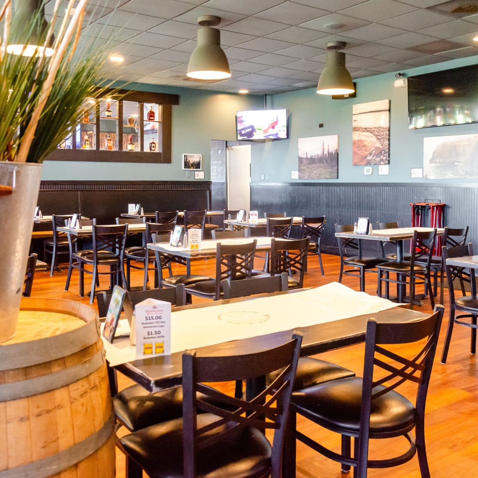 Interior of a restaurant with empty tables and chairs, wood floors, and light blue walls.