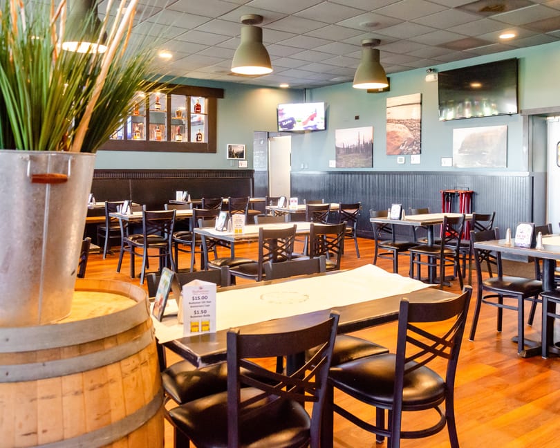 Interior of a restaurant with empty tables and chairs, wood floors, and light blue walls.