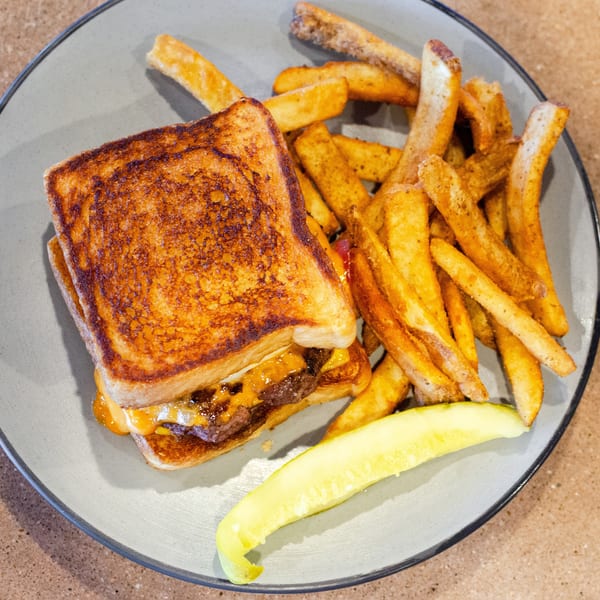 Grilled cheese burger with fries and a pickle spear on a gray plate.