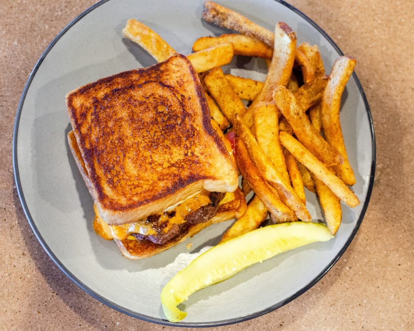Grilled cheese burger with fries and a pickle spear on a gray plate.