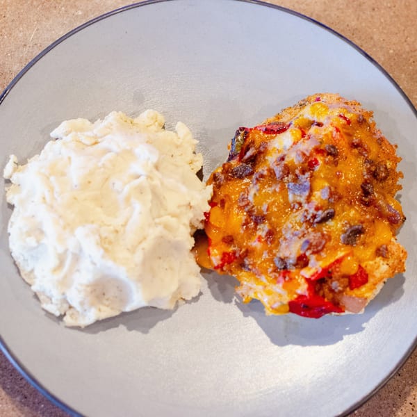 A plate of mashed potatoes next to a cheesy casserole with red peppers and meat.