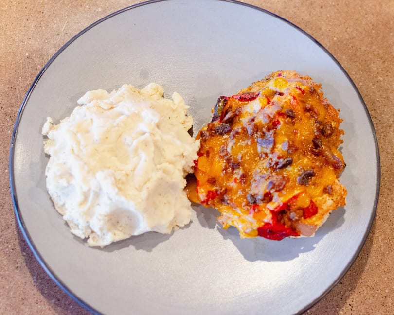 A plate of mashed potatoes next to a cheesy casserole with red peppers and meat.
