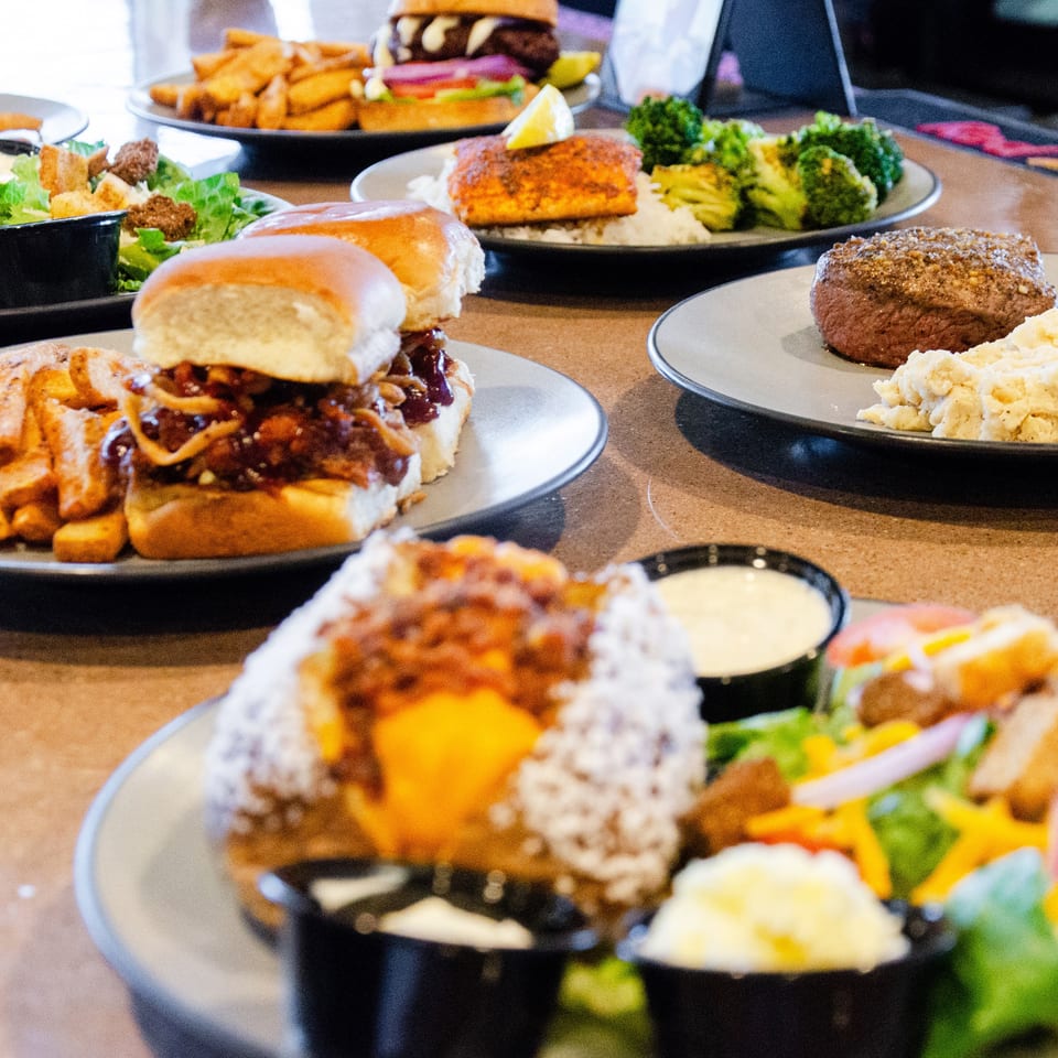 A table filled with various dishes including sliders, steak, salmon, salads, and fries.