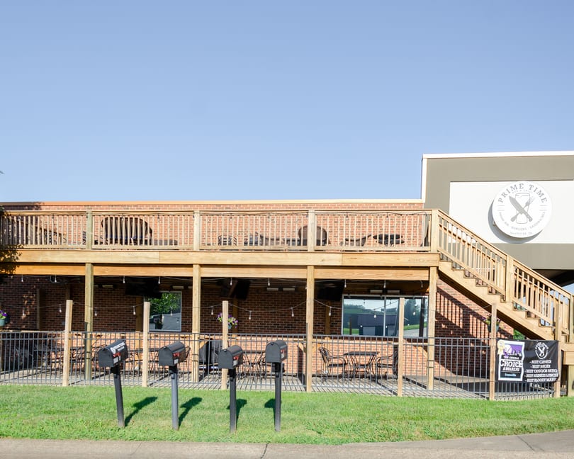 Exterior of Prime Time Pub & Grill, showing a two-story brick building with outdoor patio seating.
