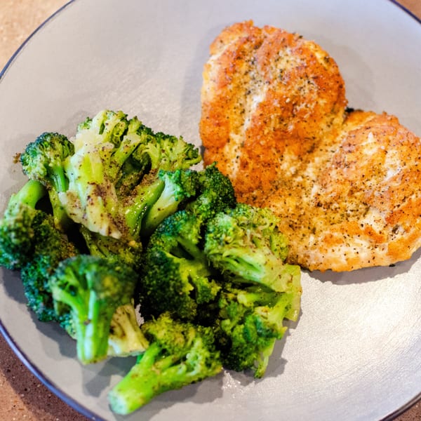Seasoned chicken breast and steamed broccoli florets on a light gray plate.