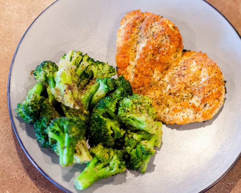 Seasoned chicken breast and steamed broccoli florets on a light gray plate.